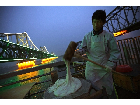 Un vendedor ambulante norcoreano prepara pan junto al puente de Dandong, en la frontera  (ANSA).