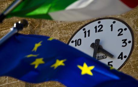 Un orologio tra due bandiere, quella Italiana e quella Europea. © ANSA 