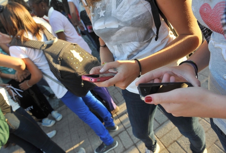 un gruppo di ragazze consulta i suoi smartphone all'uscita da scuola © ANSA