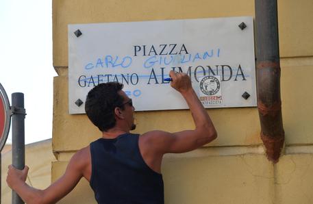 Un ragazzo scrive con un pennarello 'Carlo Giuliani' al posto di 'Gaetano Alimonda' sulla targa  della piazza durante la commemorazione della morte del ragazzo nel 2015 © ANSA 