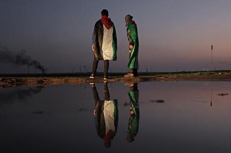 Due palestinesi che protestano riflessi in una pozza durante i bombardamenti tra Israele e la Striscia di Gaza © EPA