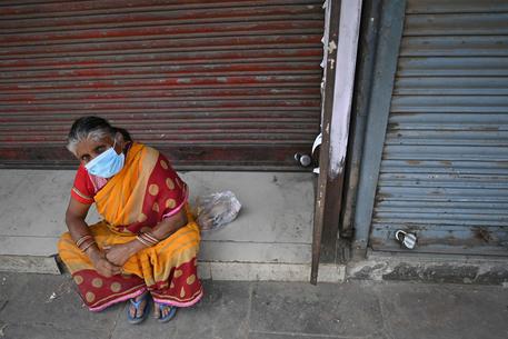 Una donna con la mascherina seduta per strada in India © AFP