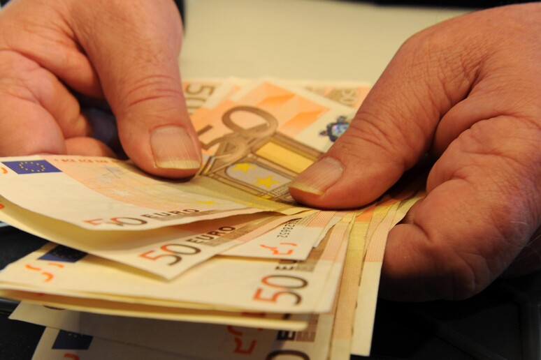 Una persona conta alcune banconote in una banca in una foto di archivio - RIPRODUZIONE RISERVATA