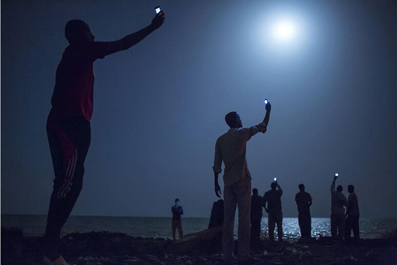 Migranti somali si riversano di notte sulle coste di Gibuti alla ricerca di un segnale gratuito per il cellulare. Fotografia di John Stanmeyer - RIPRODUZIONE RISERVATA