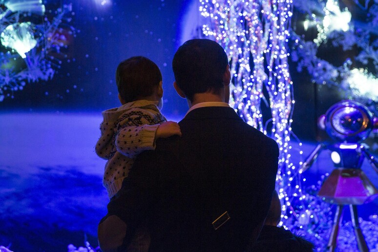 Un uomo con un bimbo in braccio osserva le luci di Natale © ANSA/EPA