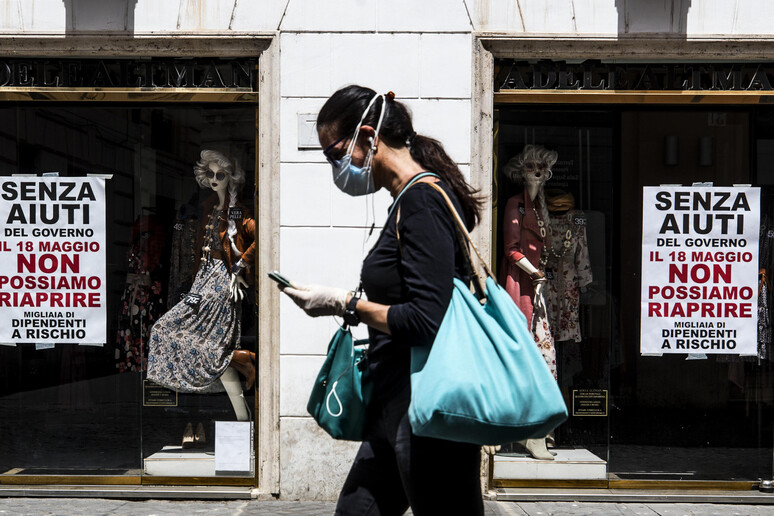 Una donna passa accanto alle vetrine di un negozio a Roma - RIPRODUZIONE RISERVATA
