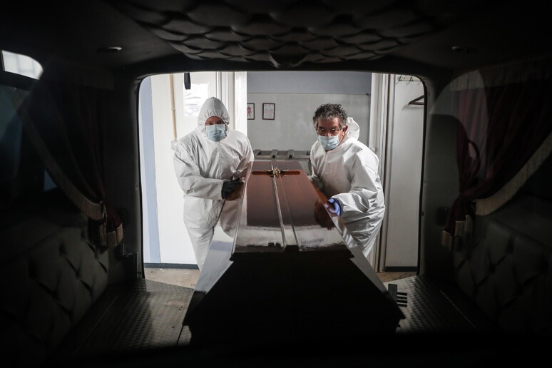 Operatori delle pompe funebri si occupano della bara di una vittima del Covid in Portogallo © ANSA/EPA
