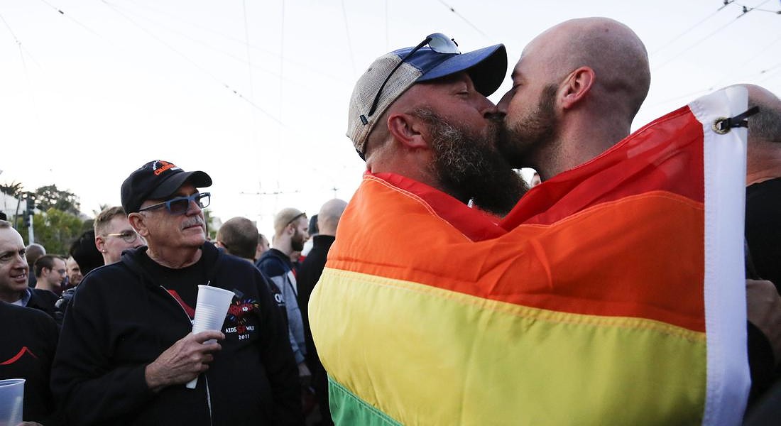 A couple shares a kiss as they embrace each other under a pride flag while residents of  San Francisco and the Bay Area © EPA