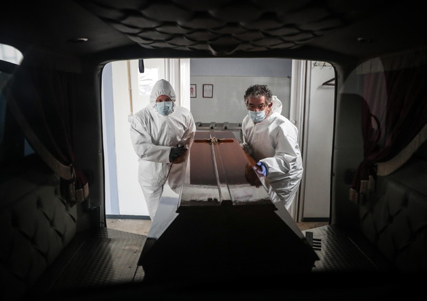 Operatori delle pompe funebri si occupano della bara di una vittima del Covid in Portogallo © EPA