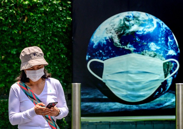 Una donna a Bangkok vicio a un cartello con la Terra con una mascherina protettiva © AFP