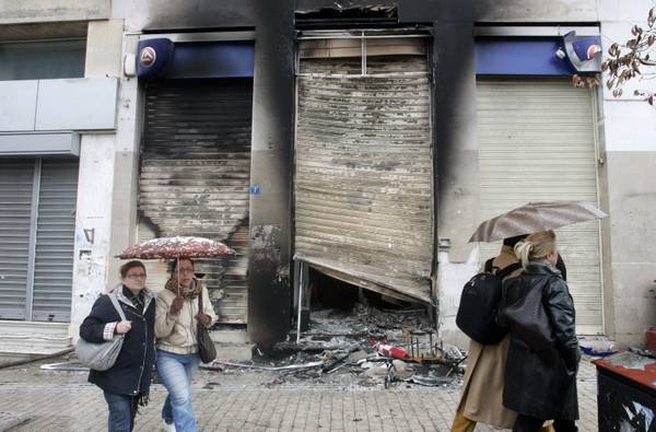 Passanti davanti a una filiale di Eurobank distrutta nelle violenze di ieri ad Atene