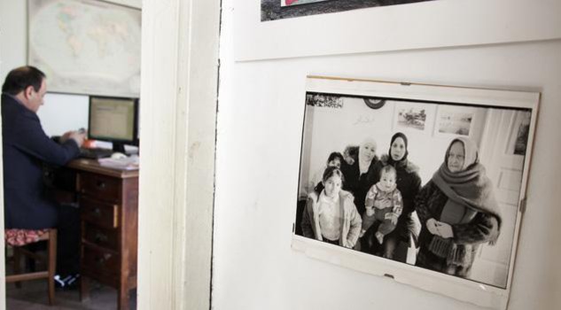 Foto di una delle prime famiglie migranti arrivate a Riace. Sullo sfondo Domenico Lucano al lavoro nell’ufficio dell’associazione “Città Futura”. © Gianfranco Ferraro