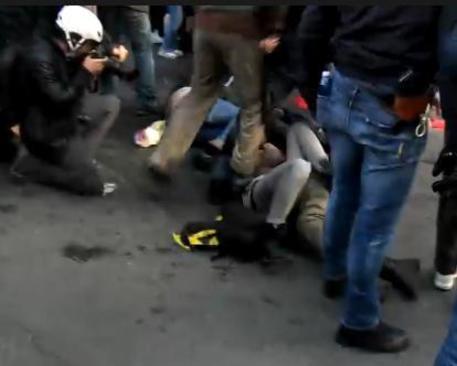 In un frame da un video esclusivo di 'Servizio Pubblico', la telecamera registra il momento in cui un agente di polizia appoggia un piede sulla pancia di una ragazza durante le proteste del corteo del 12 aprile a Roma © ANSA