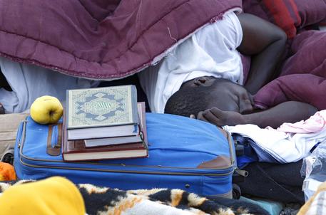 Un migrante dorme accanto al Corano sugli scogli a Ventimiglia © AP