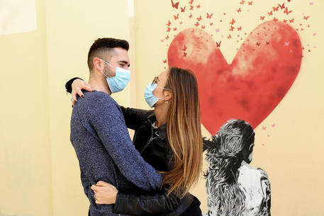 Una coppia di fidanzati con mascherina anti contagio si abbraccia davanti ad un murales a Padova. FOTO NICOLA FOSSELLA © ANSA