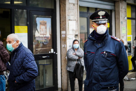 Un carabiniere controlla il rispetto della distanza di sicurezza di persone in fila alla posta © ANSA