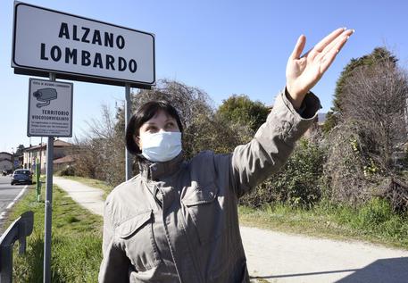 Il cartello d'ingresso al comune di Alzano e una signora con la mascherina. © 