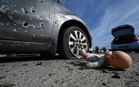 Una bambola accanto ad una macchina perforata da proiettili a Irpin © AFP