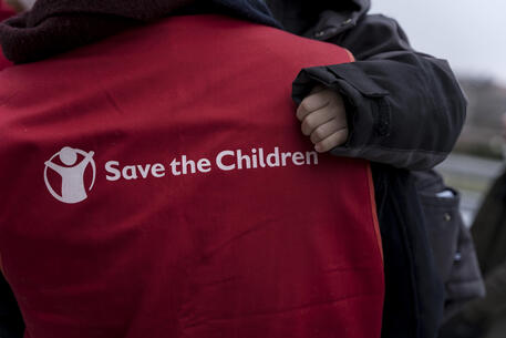 Un operatore di Save the Children con in braccio un bambino © ANSA