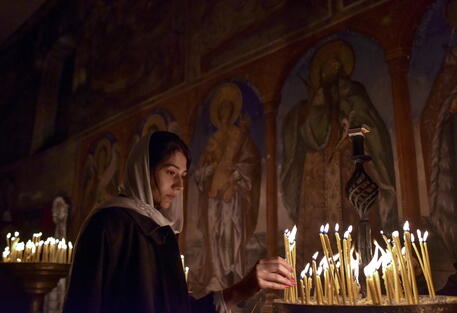 Una donna accende una candela in una chiesa © EPA