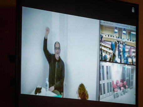 Cospito saluta i suoi sostenitori da un mega schermo durante il processo a suo carico - Foto di archivio © ANSA