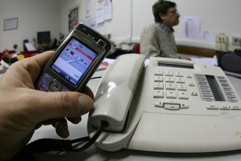 Una persona  tiene in mano un cellulare vicino a un telefono di rete fissa. Foto d 'archivio ANSA / FRANCO SILVI - RIPRODUZIONE RISERVATA