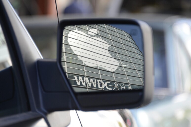 Il logo Apple riflesso in uno specchietto retrovisore - RIPRODUZIONE RISERVATA