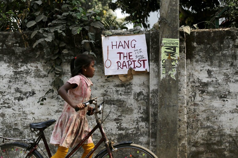 Una ragazza indiana in bicicletta passa vicino un manifesto con la scritta  'Impiccate il violentatore ' (archivio) © ANSA/EPA