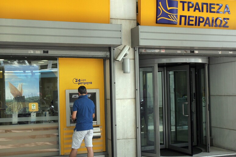 Un uomo preleva contanti da un distributore della Banca del Pireo ad Atene -     RIPRODUZIONE RISERVATA