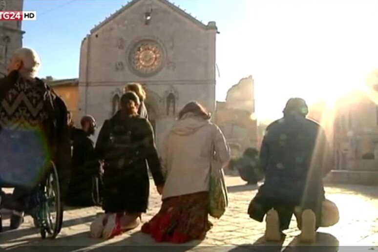 Persone in preghiera davanti la basilica di San Benedetto distrutta dal forte terremoto - RIPRODUZIONE RISERVATA