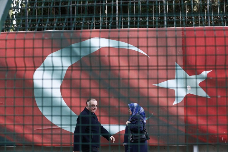 Due persone davanti ad una bandiera turca © ANSA/EPA
