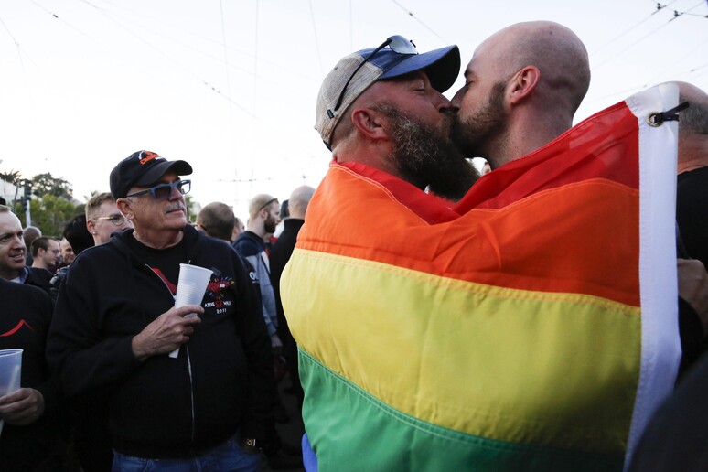 A couple shares a kiss as they embrace each other under a pride flag while residents of  San Francisco and the Bay Area © ANSA/EPA