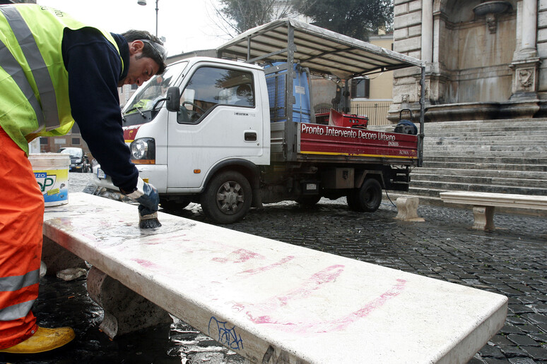 Un addetto dell 'Ama toglie le scritte da una panchina a Roma - RIPRODUZIONE RISERVATA
