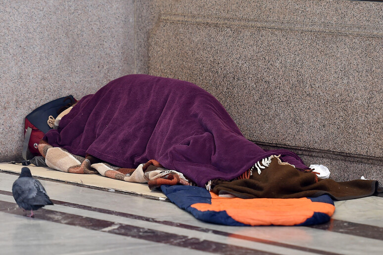 Un clochard dorme in un sacco a pelo sotto i portici delle vie centrali di Torino - RIPRODUZIONE RISERVATA