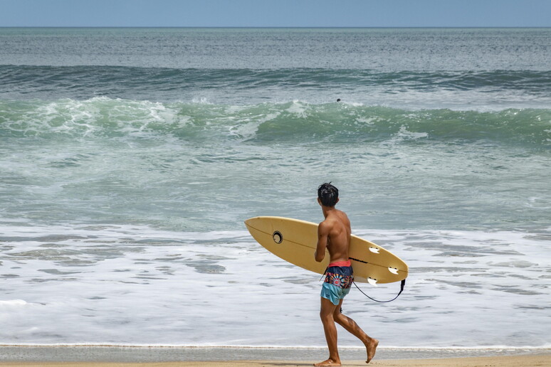 Un turista con una tavola da surf - RIPRODUZIONE RISERVATA