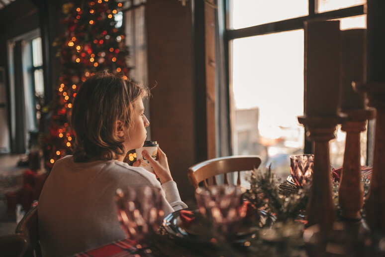 Un giovane teenager guarda la finestra in solitudine a Natale, foto iStock. - RIPRODUZIONE RISERVATA