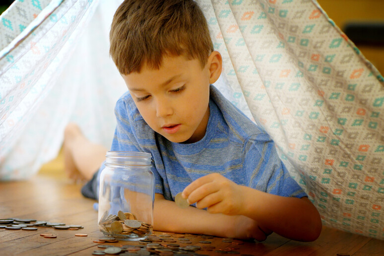 Little boy adding coins to jar. - RIPRODUZIONE RISERVATA