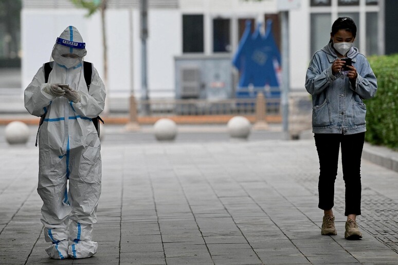 Un operatore sanitario e una passante con la mascherina in strada in Cina (foto d 'archivio) © ANSA/AFP