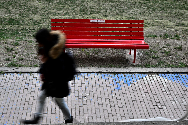 Una ragazza cammina davanti ad una panchina rossa (archivio) - RIPRODUZIONE RISERVATA