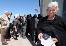 Una donna anziana mostra il  libretto di risparmio, davanti a una filiale della Banca Laik a Nicosia